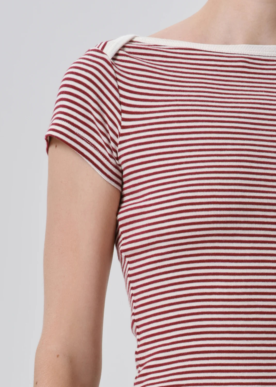 Close-up of a person wearing a short-sleeve ribbed top with horizontal red and off-white stripes, cropped from the neck to the upper torso against a light gray background.