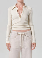 Person wearing a cream-colored long-sleeve shirt with a collar and light pink pants on a gray background