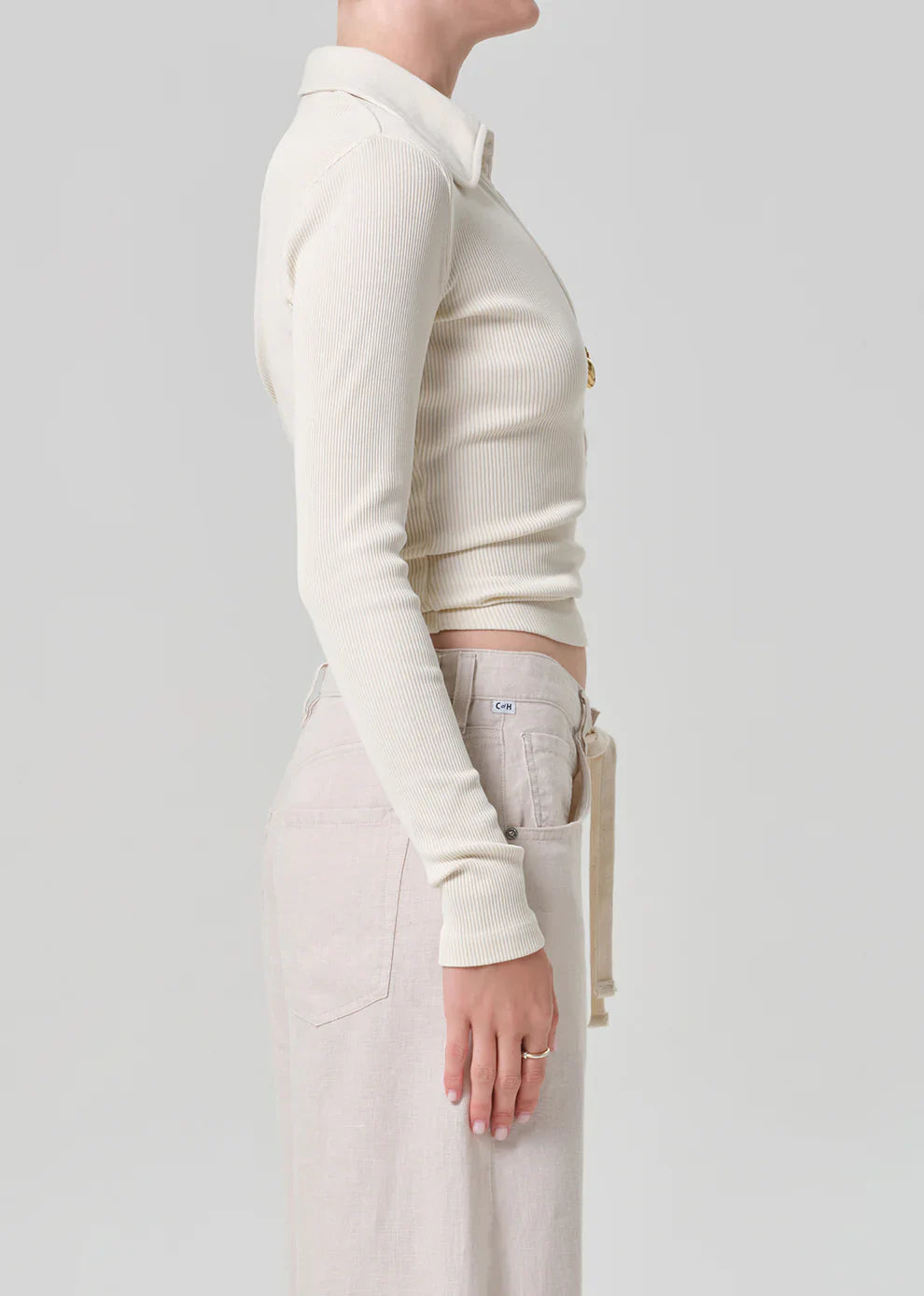 Person wearing a cream-colored long-sleeve top and light-colored pants on a plain background