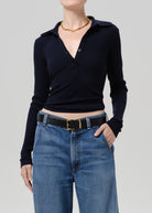 A model wearing a dark navy long-sleeve polo shirt tucked into blue jeans with a black belt, shown from the neck down against a solid gray studio background.
