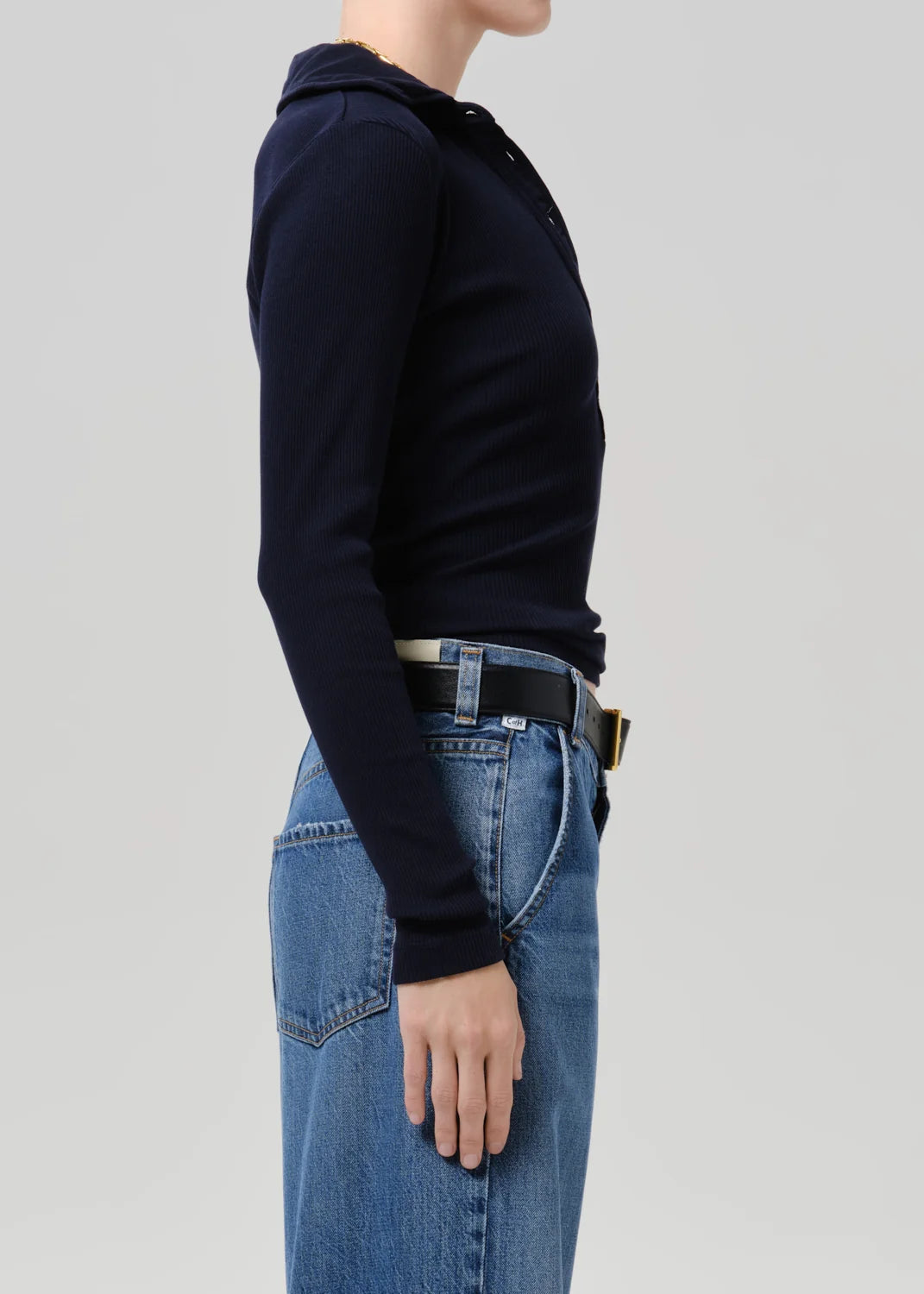 Side profile of a model wearing a dark navy long-sleeve knit polo hoodie tucked into blue jeans with a black belt.