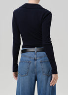 A model shown from the back wearing a dark navy long-sleeve knit top tucked into blue jeans with a black belt, against a solid light gray background.