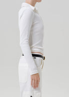 Side profile of a model wearing a white long-sleeve ribbed knit polo shirt tucked into white cargo pants with a black belt.
