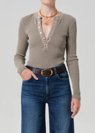 Person wearing a brown long-sleeve henley shirt and blue jeans on a plain background