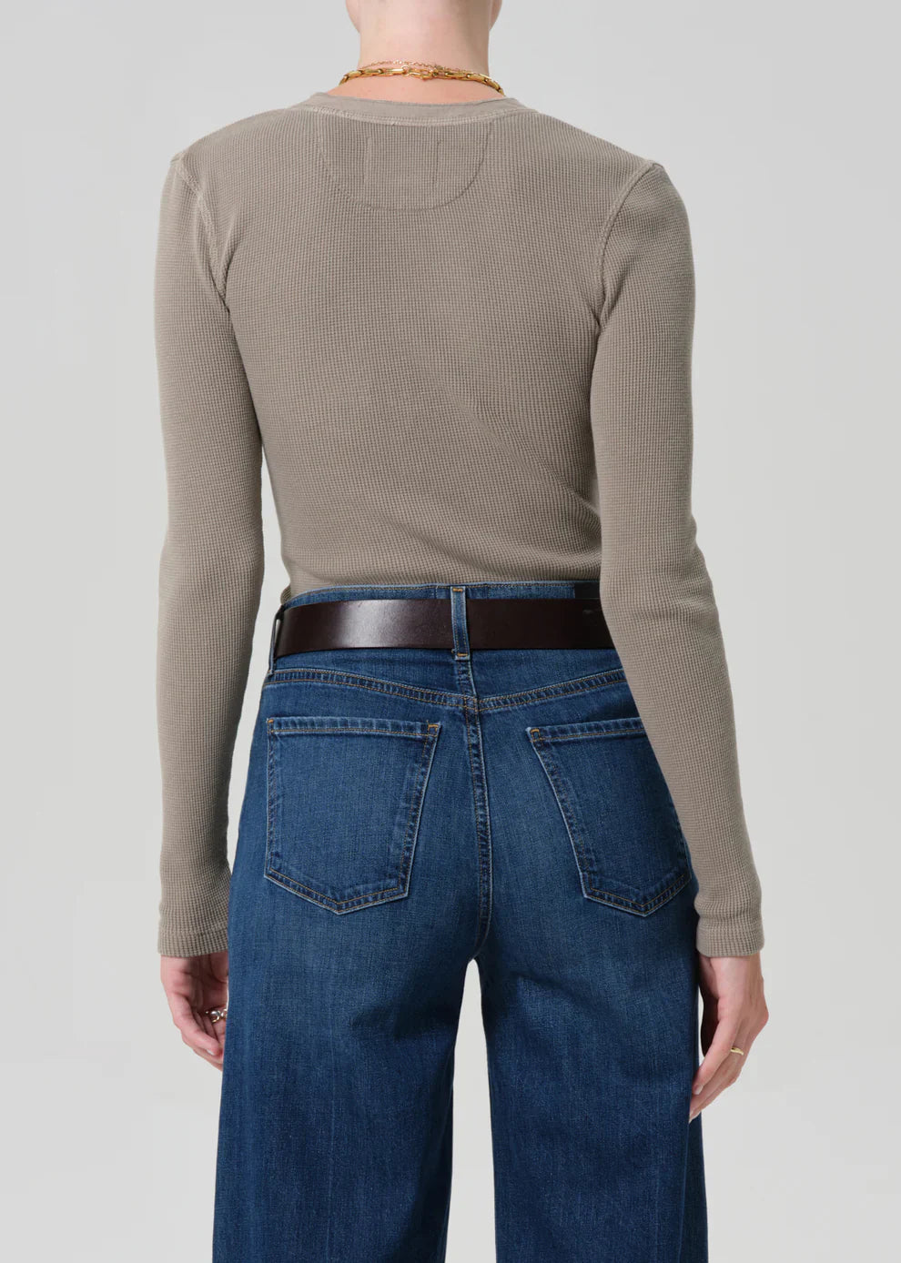 Person wearing a beige long-sleeve shirt and blue jeans on a plain background