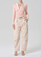 Person wearing a pink sweater and beige pants on a white background