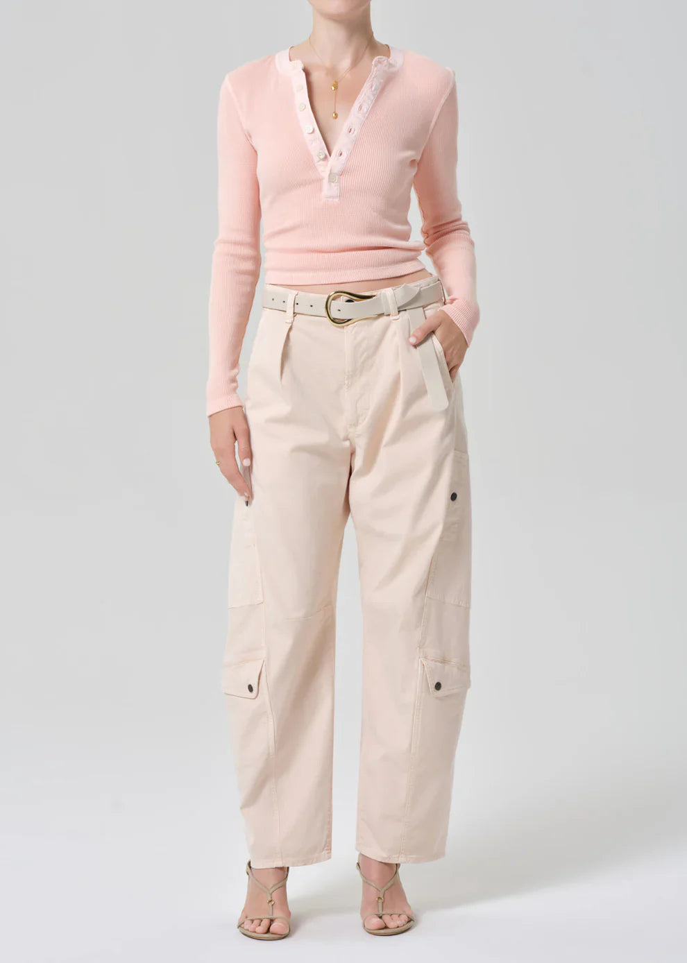 Person wearing a pink sweater and beige pants on a white background
