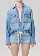Person wearing a light blue denim shirt and shorts on a plain background