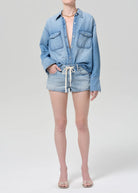 Person wearing a light blue denim shirt and shorts on a white background