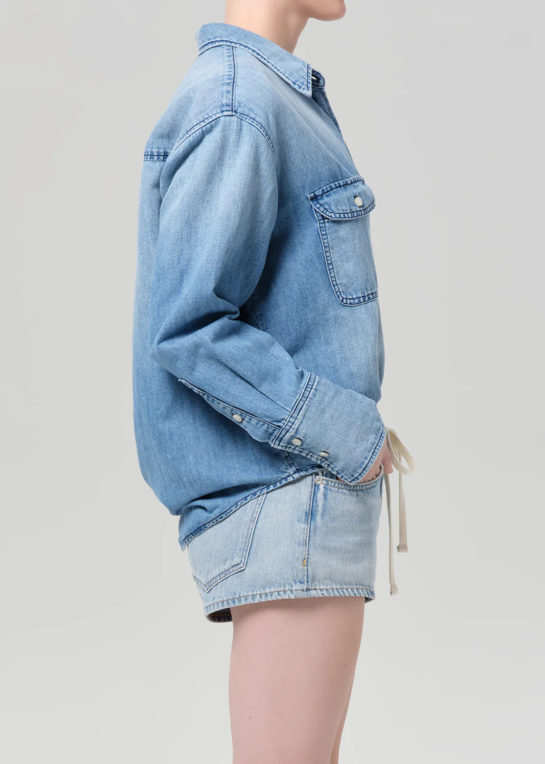 Person wearing a light blue denim jacket and shorts on a plain background