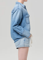 Person wearing a light blue denim jacket and shorts on a plain background