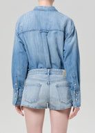 Person wearing a light blue denim jacket and shorts on a plain background