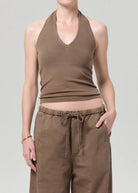 Person wearing a brown ribbed tank top and brown pants on a gray background