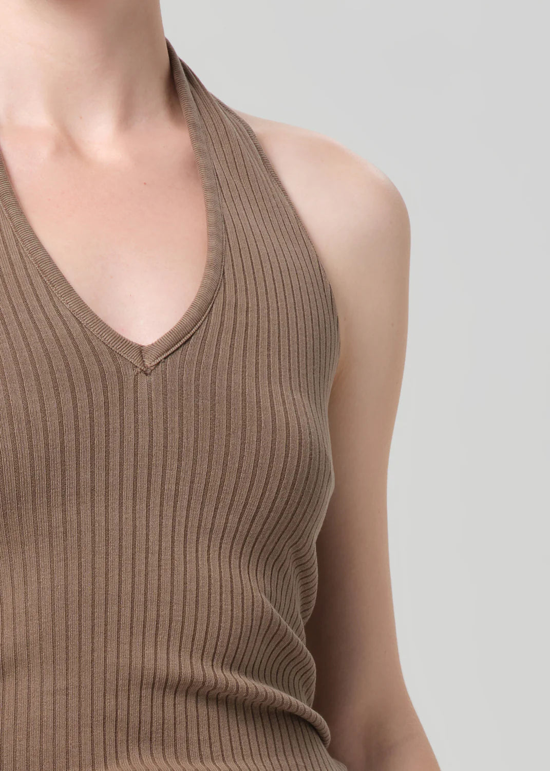 Person wearing a brown ribbed v neck halter tank top  on a gray background