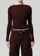 A model wearing a dark burgundy ribbed long-sleeve top with shoulder details, paired with matching dark brown cargo pants and a black belt with a gold buckle, against a solid light gray background.