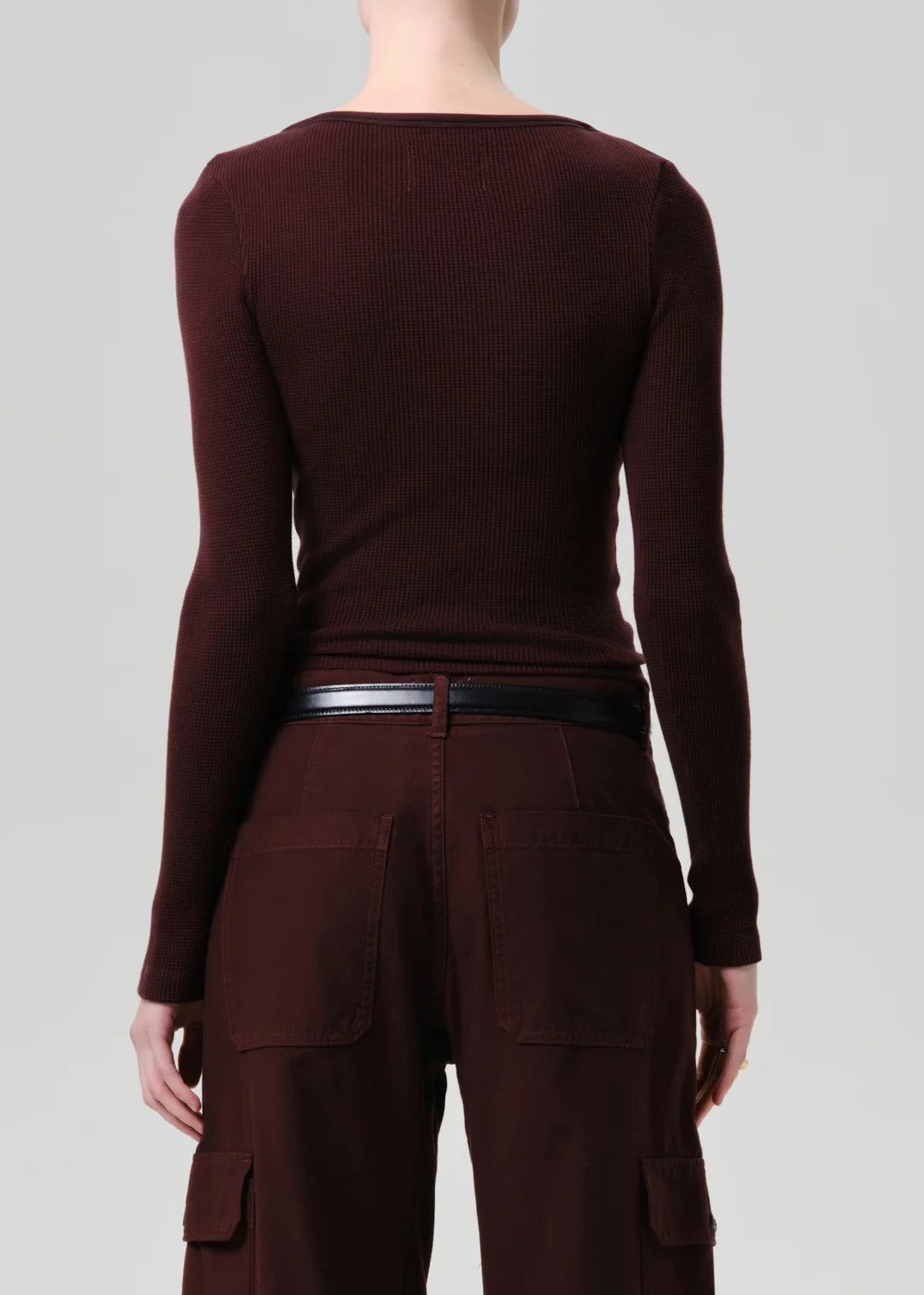 Rear view of a model wearing a dark burgundy ribbed long-sleeve top and matching cargo pants with a thin black belt, against a light gray studio background.