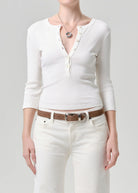 Person wearing a white long-sleeve top and white pants with a brown belt on a gray background