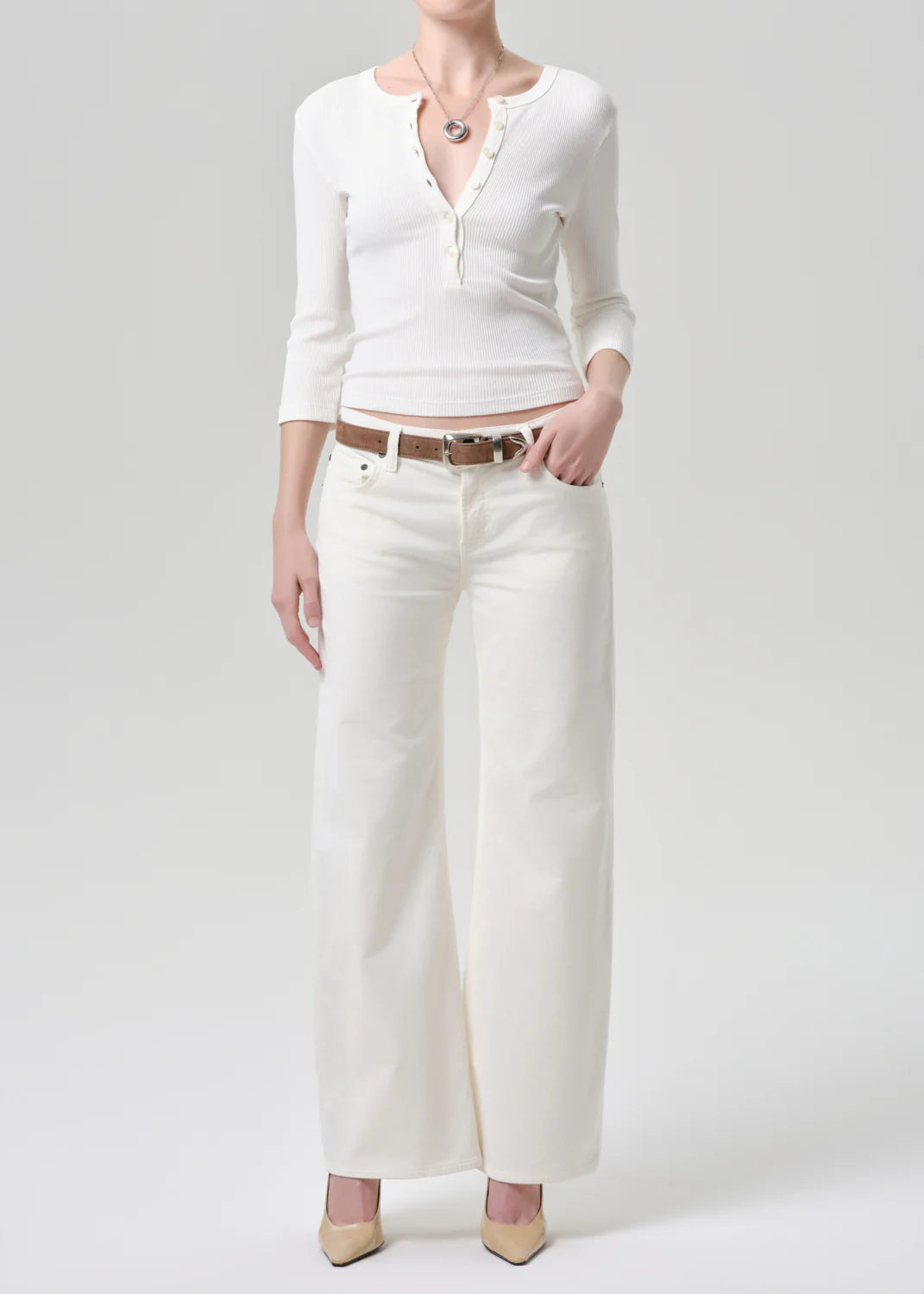 Person wearing a white cardigan, white pants, and beige shoes on a light gray background