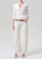 Person wearing a white cardigan, white pants, and beige shoes on a light gray background