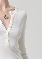 White ribbed sweater with buttons and a necklace on a plain background