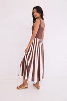 Woman wearing a brown sleeveless top and striped pants on a white background