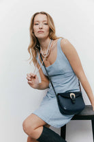 Woman in a light blue dress holding a navy handbag against a white background