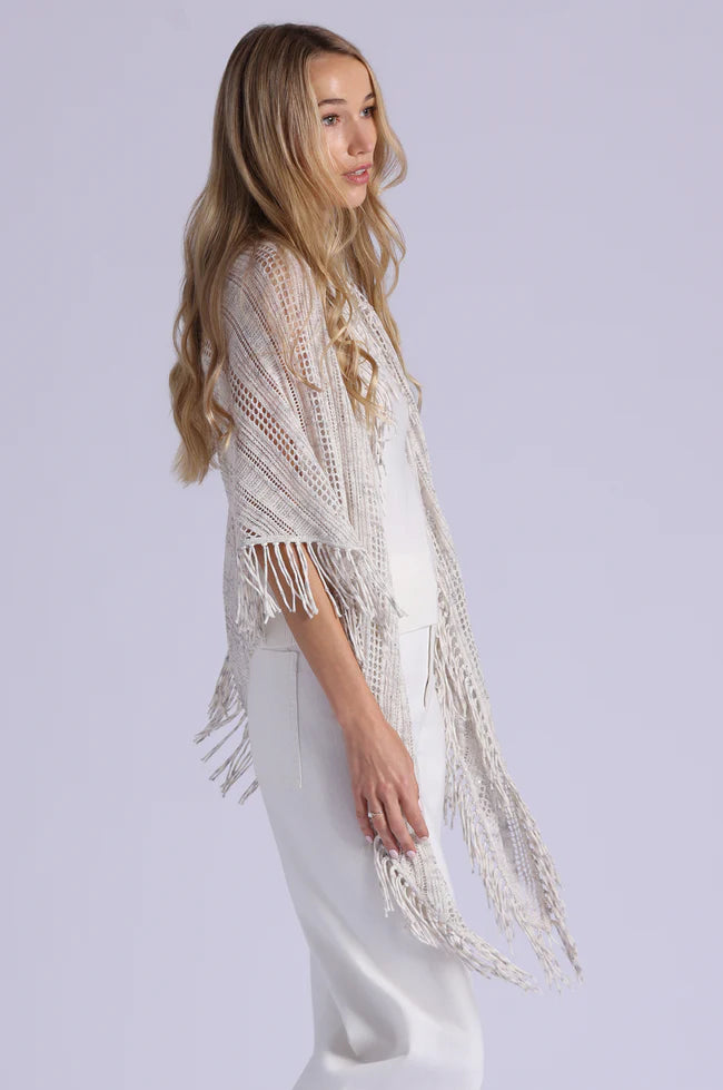 Woman wearing a beige knitted shawl with fringe on a plain background