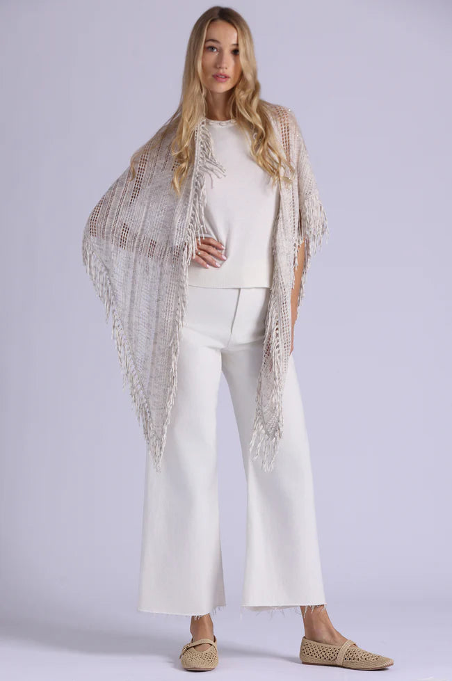 Woman wearing a white outfit with a beige lace shawl on a plain background