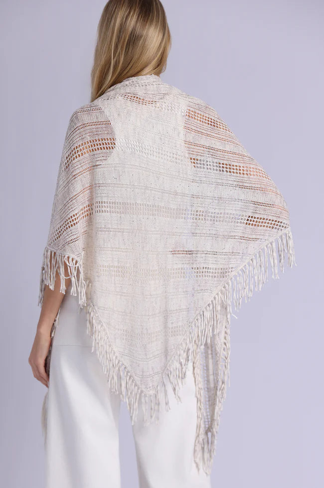 Woman wearing a beige knitted shawl with fringe on a plain background