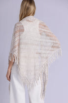 Woman wearing a beige knitted shawl with fringe on a plain background