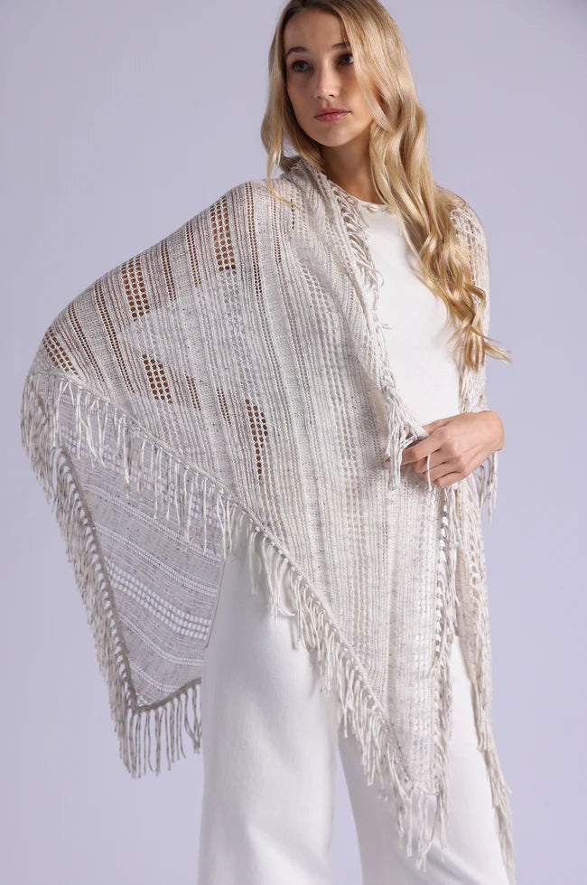 Woman wearing a beige knitted shawl with fringe on a plain background