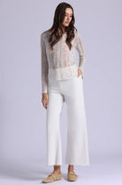 Woman wearing a sheer top and white pants on a light gray background