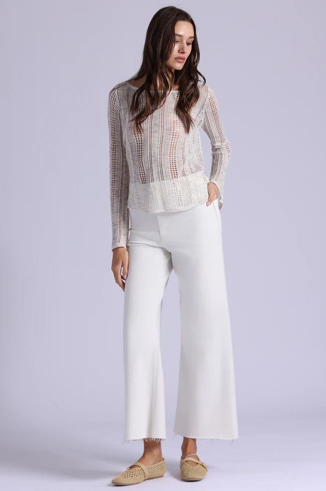 Woman wearing a sheer top and white pants on a light gray background