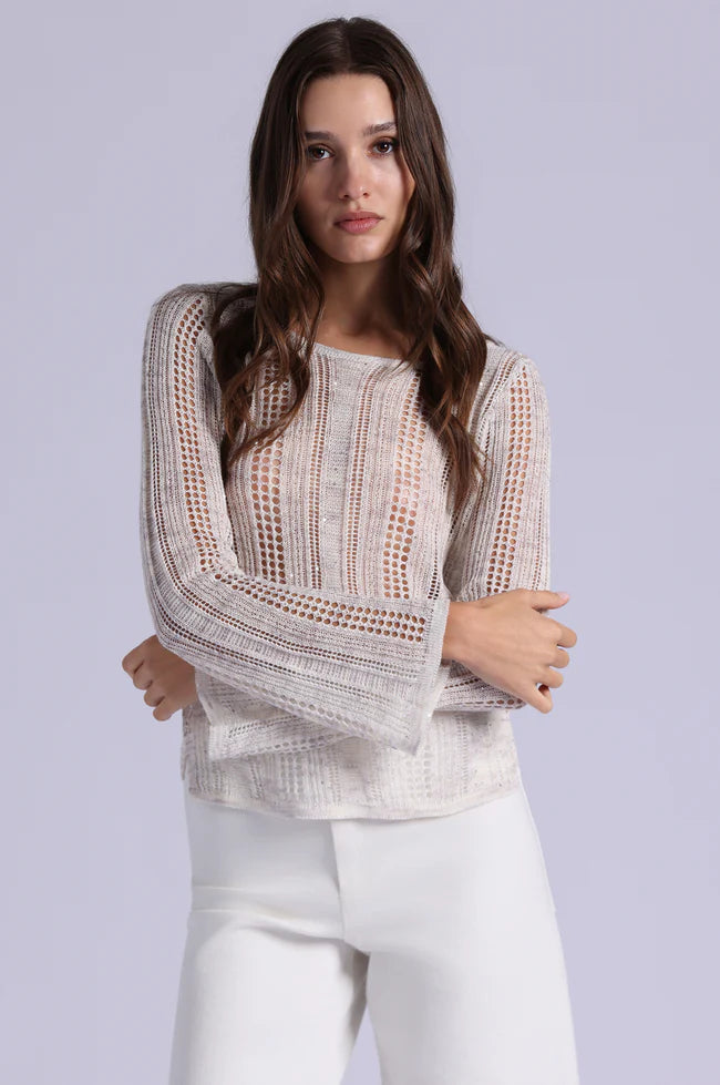 Woman wearing a beige crochet top and white pants against a light gray background