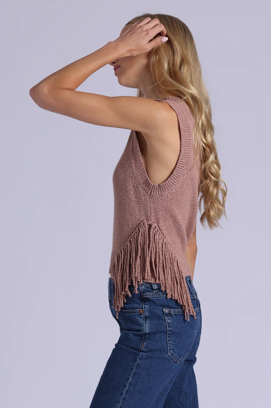 Woman wearing a brown fringe tank top and blue jeans against a light gray background