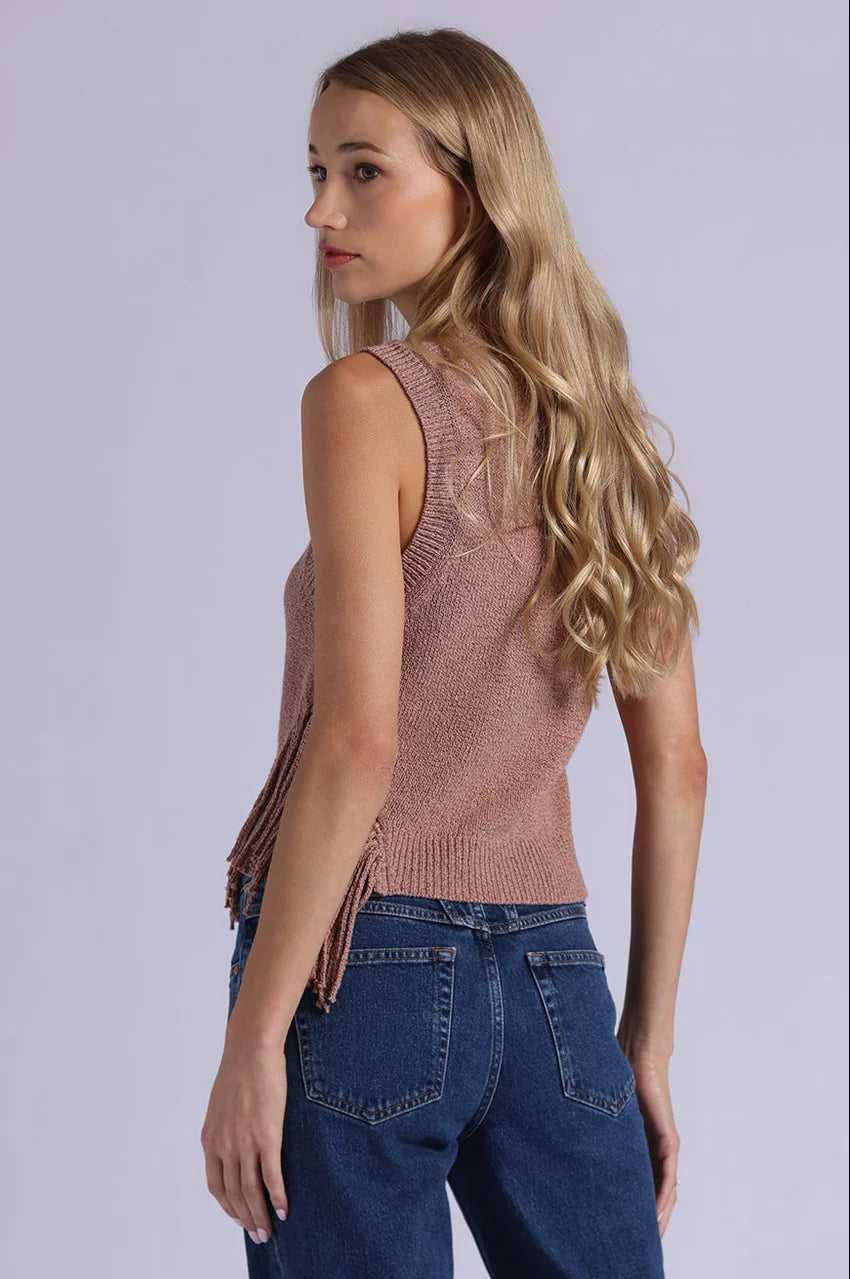 Woman wearing a sleeveless knitted top and blue jeans on a plain background