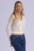 Woman wearing a white knit cardigan over a white shirt with blue jeans on a light gray background