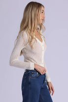 Woman wearing a beige ribbed sweater and blue jeans on a light gray background