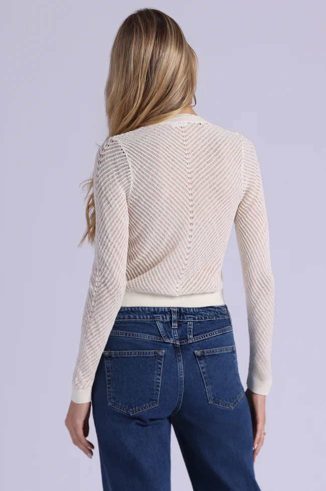 Woman wearing a beige ribbed sweater and blue jeans on a light gray background
