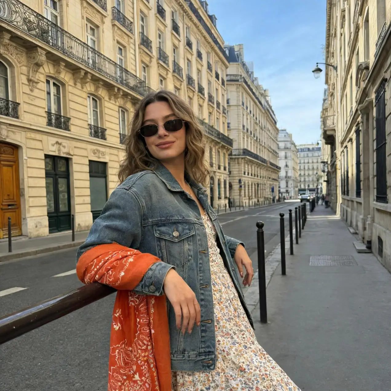 Woman in a denim jacket and floral dress standing on a city street.