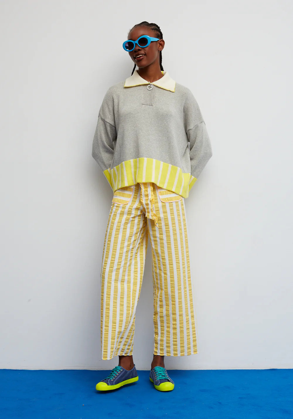 Person wearing a gray sweater with a yellow collar and striped pants on a white background