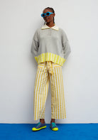 Person wearing a gray sweater with a yellow collar and striped pants on a white background