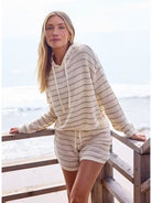 Woman wearing a beige crochet hoodie and shorts set by the ocean.