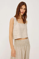 Woman wearing a beige sleeveless top and pants on a white background