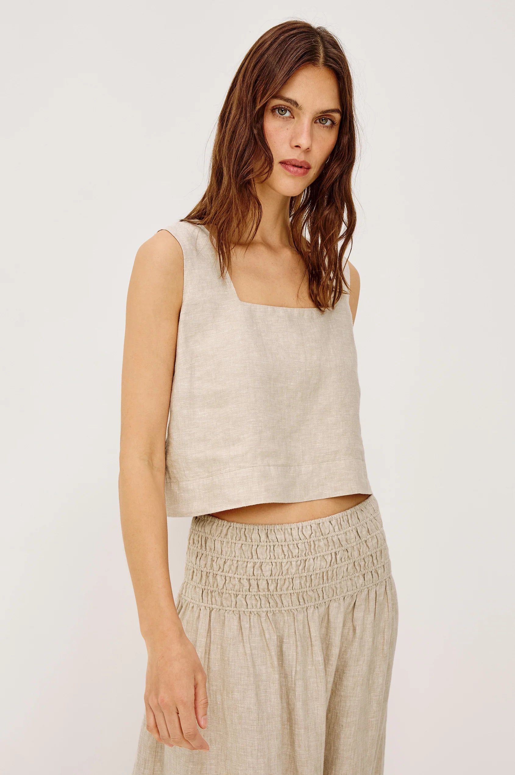 Woman wearing a beige sleeveless top and pants on a white background