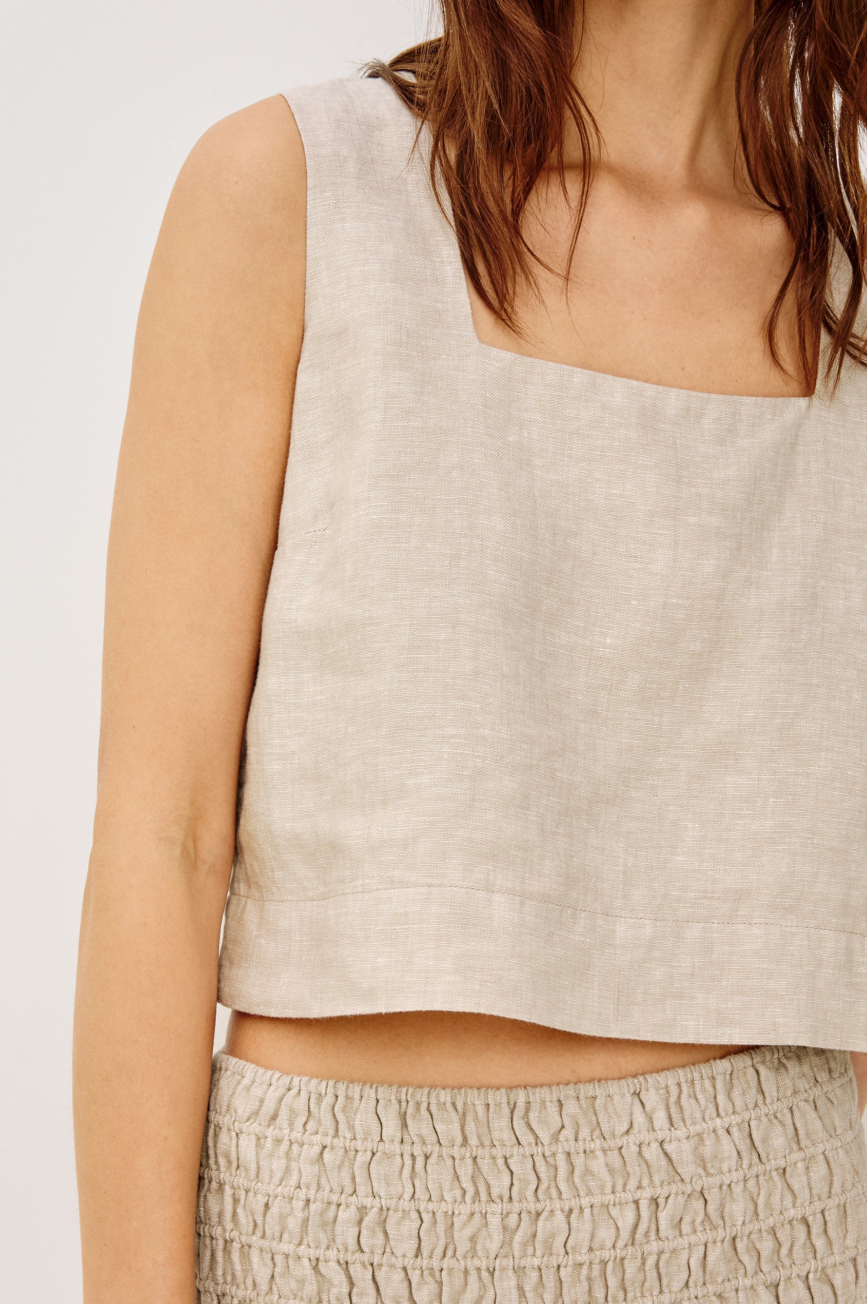 Beige sleeveless top worn by a person on a white background