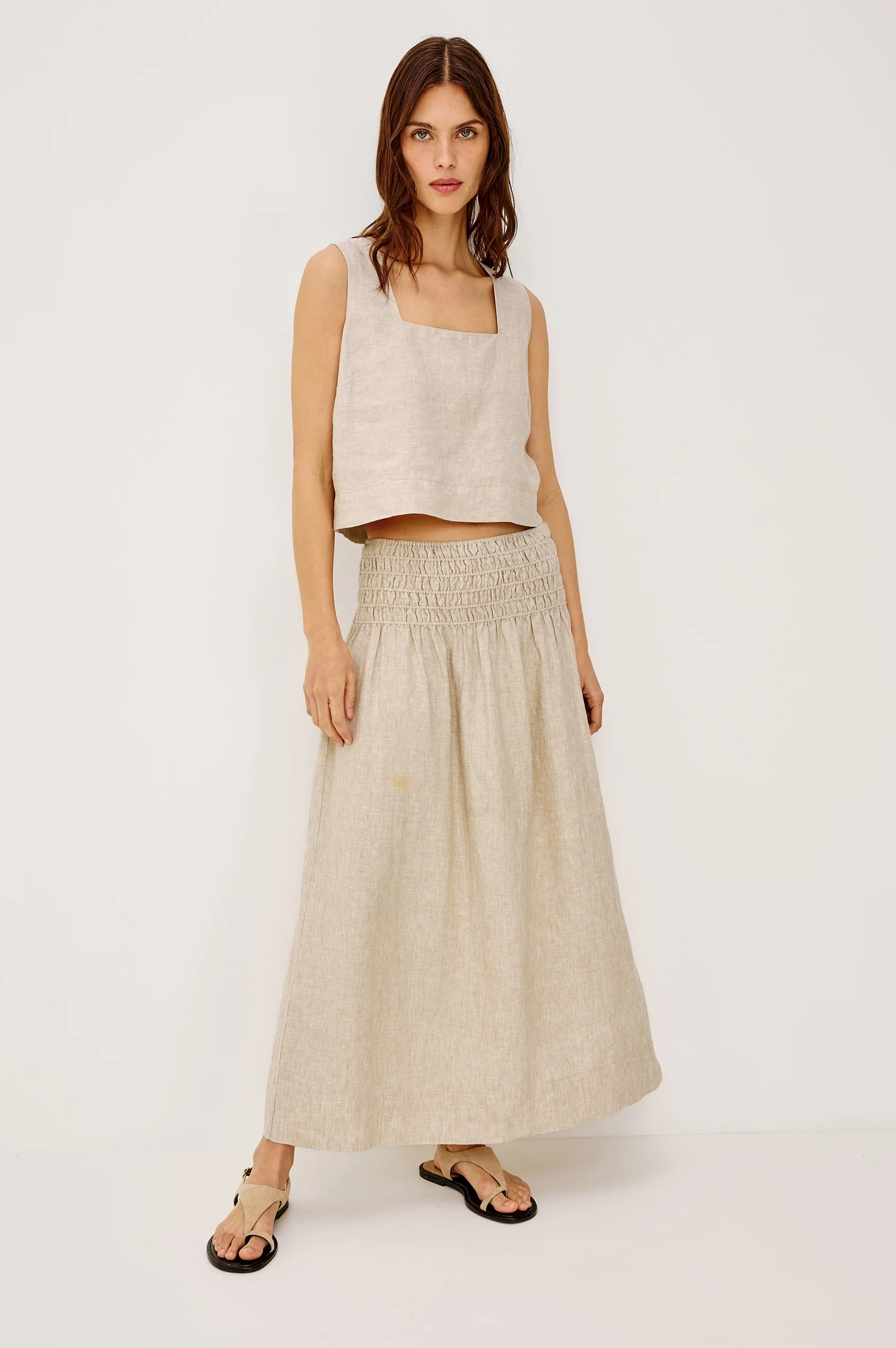 Woman wearing a beige sleeveless top and long skirt on a white background