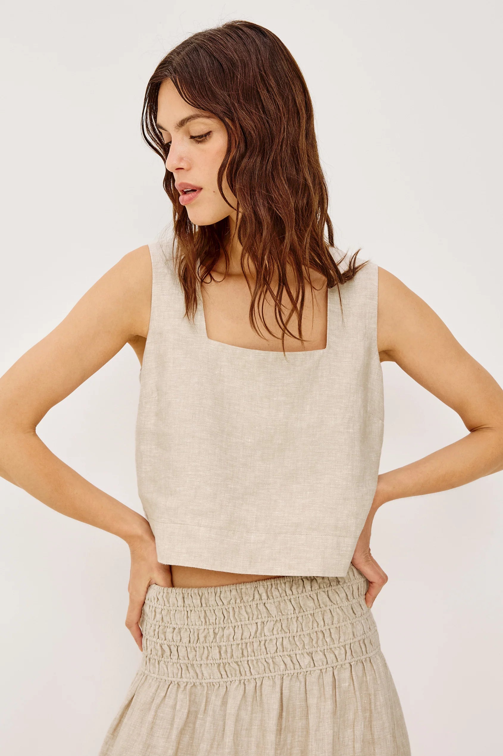 Woman wearing a beige sleeveless top and skirt against a white background