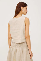 Woman wearing a beige sleeveless top and skirt set on a plain background