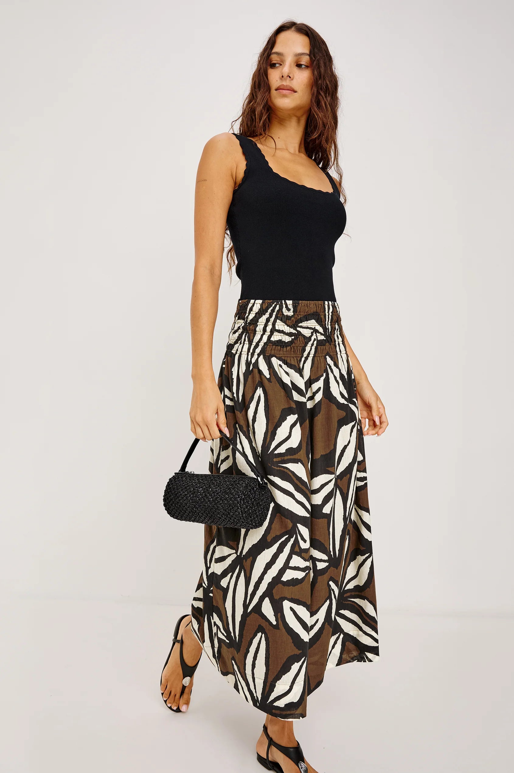 Woman wearing a black top and zebra print skirt with a black handbag on a white background